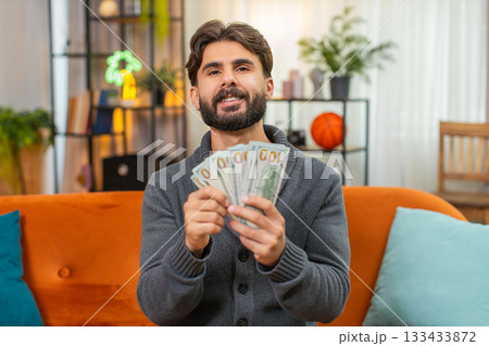 Indian man counts dollar cash banknotes dreams of travel thinks where to spend money smiles wealthy 133433872