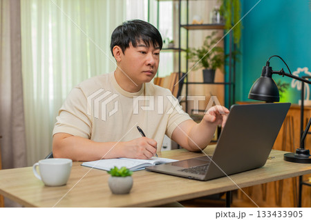 Asian man taking notes from online course on laptop, explaining to camera with clear confident tone 133433905