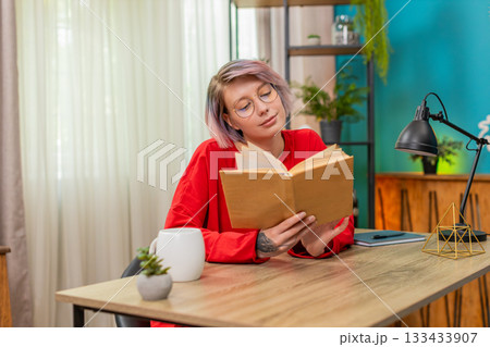 Young woman thoughtfully reading book turning pages concentrated serious expression literature hobby Young woman thoughtfully reading book turning pages concentrated serious expression literature hobby 133433907