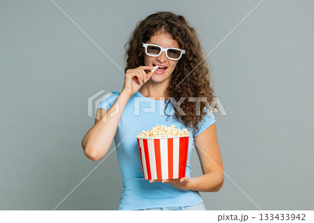 Woman watching exciting movie in 3D glasses eating popcorn, emotional surprised amazed reaction Woman watching exciting movie in 3D glasses eating popcorn, emotional surprised amazed reaction 133433942