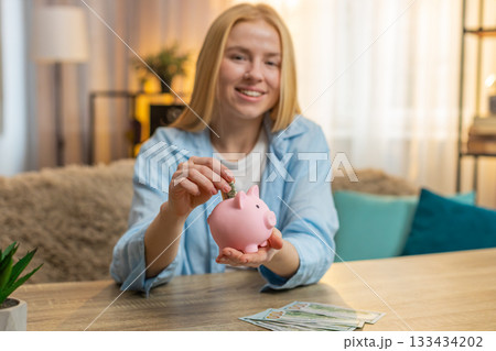 Young smiling woman saving money at home, piggy bank deposit, future planning, satisfied mindset Young smiling woman saving money at home, piggy bank deposit, future planning, satisfied mindset 133434202