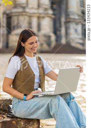 Caucasian young woman freelancer working online distant job with laptop sitting on city town street Caucasian young woman freelancer working online distant job with laptop sitting on city town street 133434213