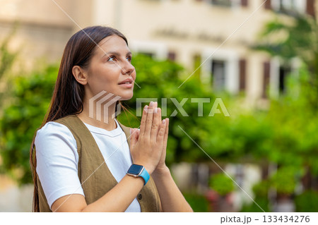 Young European woman praying with closed eyes to god asking for blessing, help, forgiveness outdoors Young European woman praying with closed eyes to god asking for blessing, help, forgiveness outdoors 133434276