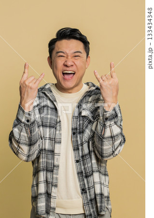 Happy Asian man showing rock n roll gesture by hands cool sign crazy expression dancing victory win 133434348