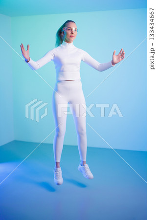 Female in smartglasses jumping against blue background 133434667