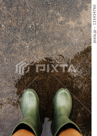 POV shot of person with rain boots standing on wet ground during rainfall, with raindrops in Rainy season 133434760