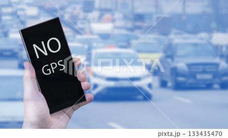 A hand with a smartphone on the background of a busy highway in a megalopolis with the inscription no GPS, the lack of a GPS signal makes it difficult to locate in an unfamiliar place. 133435470