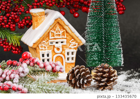 Gingerbread style ceramic Christmas house with pine cone, holly berries and snowy winter tree Gingerbread style ceramic Christmas house with pine cone, holly berries and snowy winter tree 133435670