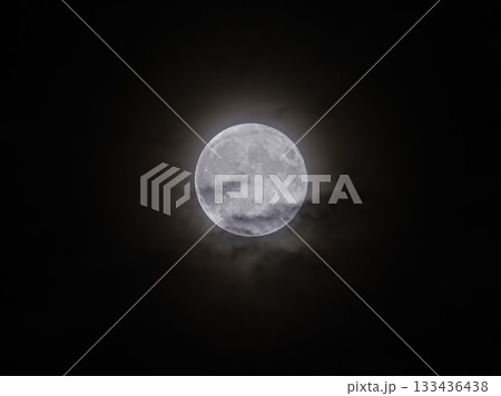 Glowing full Moon shines brightly in the dark Night Sky with a soft atmospheric Halo around it, captured from Earth. 133436438