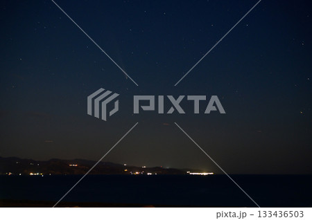 Starry night sky over the serene coastline with distant lights twinkling along the shore and a comet trailing through the cosmos Starry night sky over the serene coastline with distant lights twinkling along the shore and a comet trailing through the cosmos 133436503