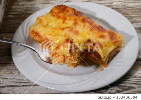 Delicious homemade lasagna served on a white plate, showcasing rich layers and melted cheese at a cozy dinner setting during evening hours 133436504