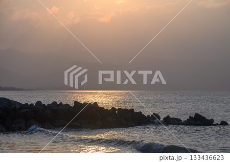 Sunset glow over calm waters with rocky coastline showcasing serene evening atmosphere on the beach Sunset glow over calm waters with rocky coastline showcasing serene evening atmosphere on the beach 133436623