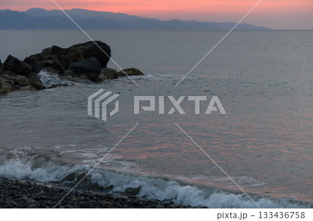 Serene sunset over tranquil waters with gentle waves lapping at rocky shorelines in a coastal landscape 133436758