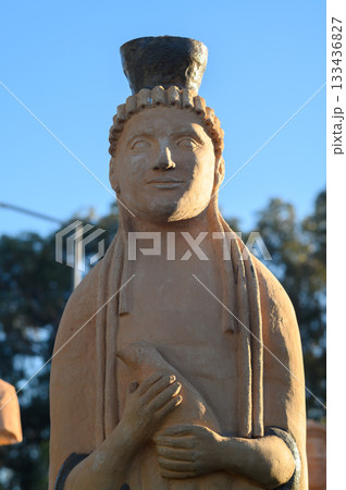 Ancient sculpture of a noble figure stands proudly against a clear blue sky in an archaeological site during the golden hour 133436827