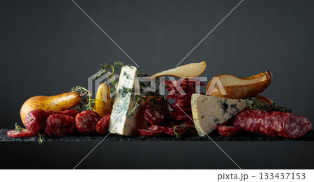 Blue cheese, dry-cured sausages, thyme and pears on a dark background. Blue cheese, dry-cured sausages, thyme and pears on a dark background. 133437153