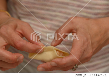 Skillful hands create delicate dumplings filled with savory goodness during a cooking session in a cozy kitchen Skillful hands create delicate dumplings filled with savory goodness during a cooking session in a cozy kitchen 133437423