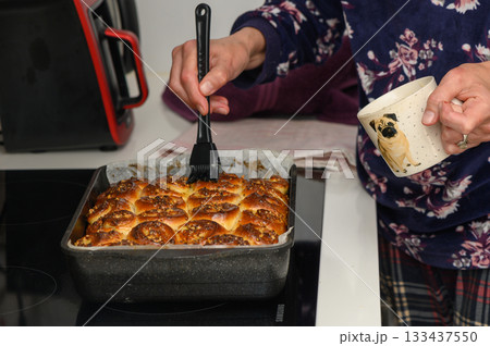 Delicious cinnamon rolls being brushed with glaze in a cozy kitchen on a chilly afternoon 133437550