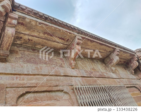 Close-up of weathered sandstone architectural detailing with carved brackets and decorative molding, showing aged texture and historic craftsmanship under cloudy sky 133438226