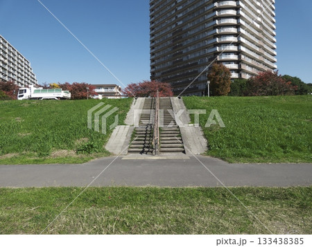 青空の下、多摩川河川敷の土手にある階段と背後にそびえる高層マンションの風景 133438385