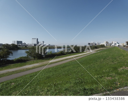 快晴の青空の下、多摩川河川敷に真っ直ぐ続くサイクリングロードと川崎側の街並み 133438386
