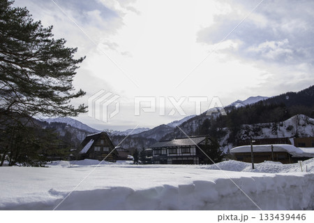 明るい雪原と伝統的な家屋、奥に山並み 明るい雪原と伝統的な家屋、奥に山並み 133439446