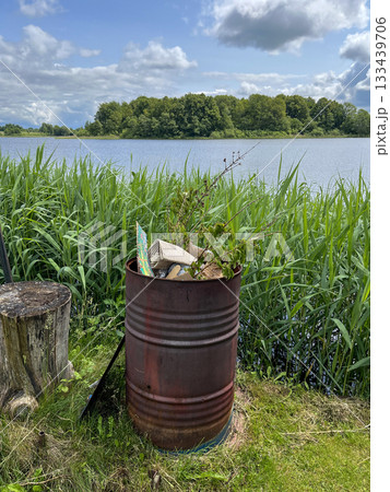 Overflowing trash barrel polluting lake shore summer nature landscape 133439706