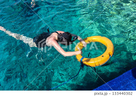A woman looks at the underwater world with her head in the water and holding onto a lifebuoy A woman looks at the underwater world with her head in the water and holding onto a lifebuoy 133440302