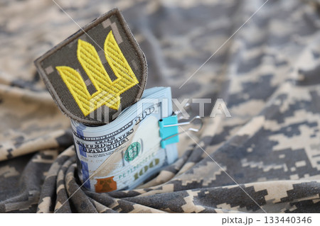 Ukrainian army symbol and bunch of dollar bills on military uniform. Payments to soldiers of the Ukrainian army from United States, salaries to the military. War support to Ukraine 133440346