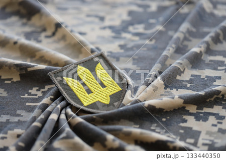 Symbol of Ukrainian army on the camouflage uniform of a Ukrainian soldier. The concept of war in Ukraine, patriotism and protecting your country from russian occupiers Symbol of Ukrainian army on the camouflage uniform of a Ukrainian soldier. The concept of war in Ukraine, patriotism and protecting your country from russian occupiers 133440350