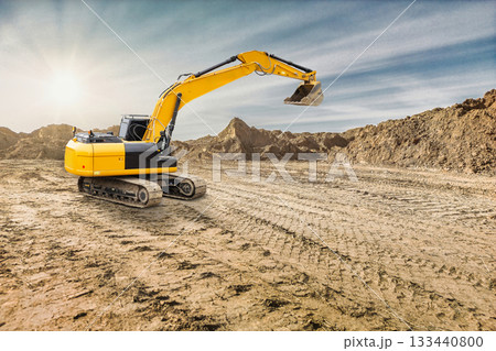 An excavator digs into the ground at a construction site during sunset, with dirt piles and a clear sky creating a serene backdrop for the project 133440800