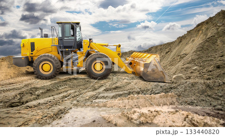 A yellow loader is seen digging and moving soil at a construction site under a dramatic sky filled with clouds on an overcast afternoon A yellow loader is seen digging and moving soil at a construction site under a dramatic sky filled with clouds on an overcast afternoon 133440820