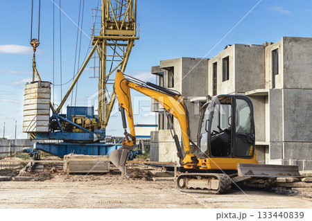 Construction activities take place with a yellow excavator and crane visible amidst partially built concrete structures under a clear blue sky 133440839