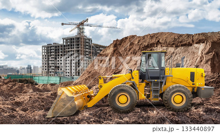 A yellow loader moves soil at a construction site where an apartment building is being built. Cloudy skies overhead hint at changing weather A yellow loader moves soil at a construction site where an apartment building is being built. Cloudy skies overhead hint at changing weather 133440897