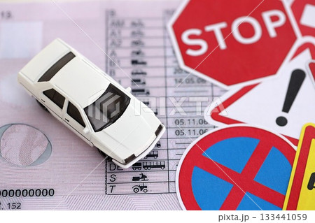 Driving school concept. Toy car and road signs on driver license close up Driving school concept. Toy car and road signs on driver license close up 133441059