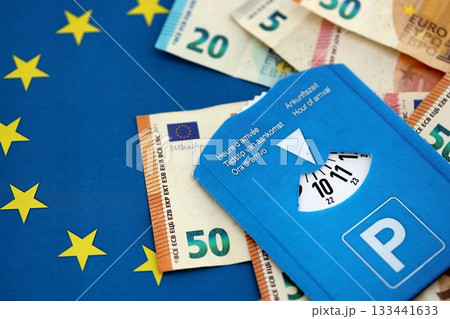 European parking disc with time dial on many euro money bills banknotes on flag of European Union. Concept of disc parking system in europe 133441633