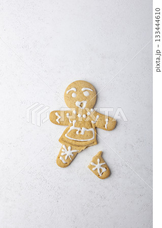 Gingerbread man with a broken leg (without leg) and with a surprised face. Traditional New Year and Christmas homemade cookies on a white background. Selective focus, close-up. Gingerbread man with a broken leg (without leg) and with a surprised face. Traditional New Year and Christmas homemade cookies on a white background. Selective focus, close-up. 133444610