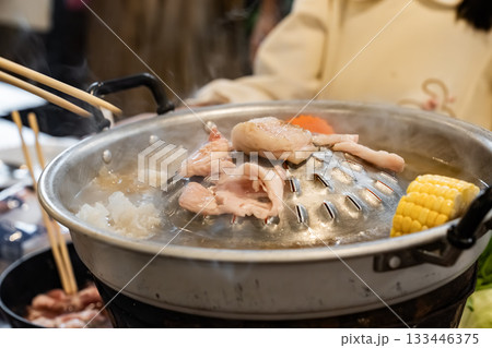 Sliced meat and vegetables cook in a metal grill pot filled with broth and steam, while the center grill browns the meat. Sliced meat and vegetables cook in a metal grill pot filled with broth and steam, while the center grill browns the meat. 133446375