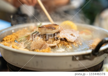 Sliced meat and vegetables cook in a metal grill pot filled with broth and steam, while the center grill browns the meat. 133446378