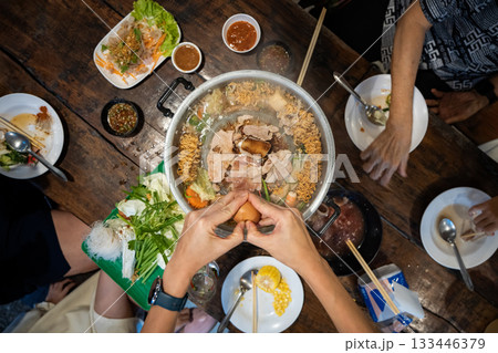 Sliced meat and vegetables cook in a metal grill pot filled with broth and steam, while the center grill browns the meat. 133446379