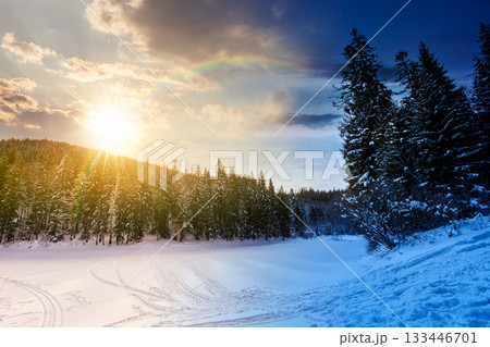 winter landscape with snow covered ground. day and night time change concept. frozen lake among spruce forest with sun and moon. panoramic view of winter wonderland. duality and transition template 133446701