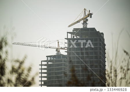 Two cranes are in the background of a building Two cranes are in the background of a building 133446928