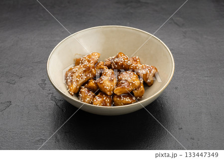 Sesame glazed chicken bites in a bowl on dark stone background 133447349