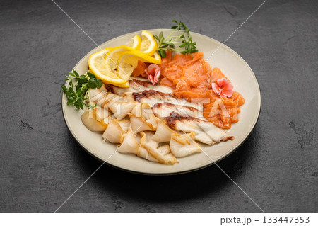 Assorted smoked fish platter with salmon, lemon slices and microgreens on plate Assorted smoked fish platter with salmon, lemon slices and microgreens on plate 133447353