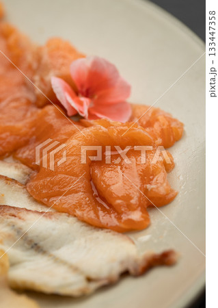 Close up of salmon sashimi with edible flower garnish on plate Close up of salmon sashimi with edible flower garnish on plate 133447358