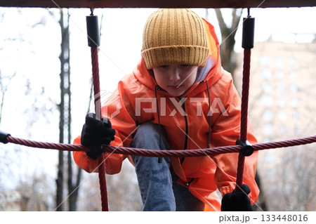 Child climbing rope net on playground in winter 133448016