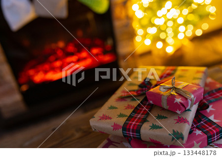 Cozy Christmas Interior with Fireplace, Gift Boxes, and Decorated Tree with Warm Lights Cozy Christmas Interior with Fireplace, Gift Boxes, and Decorated Tree with Warm Lights 133448178