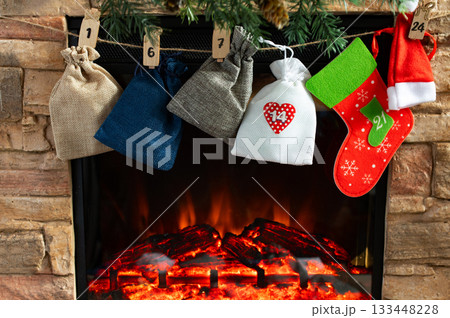 Advent Calendar Bags and Christmas Stockings Hanging Above Cozy Fireplace Advent Calendar Bags and Christmas Stockings Hanging Above Cozy Fireplace 133448228