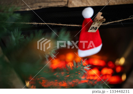 Santa Hat With Number 24 Hanging on Advent Garland Above Cozy Christmas Fireplace Santa Hat With Number 24 Hanging on Advent Garland Above Cozy Christmas Fireplace 133448231