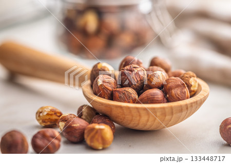 Peeled hazelnut kernels on wooden spoon on kitchen table. 133448717