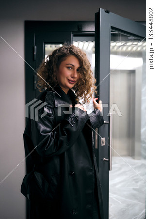 Confident woman in trench coat opening elevator door 133448802
